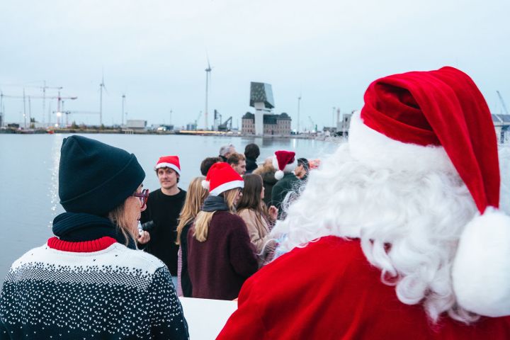 People in Santa hats gathered on a boat, festive atmosphere with waterfront view.