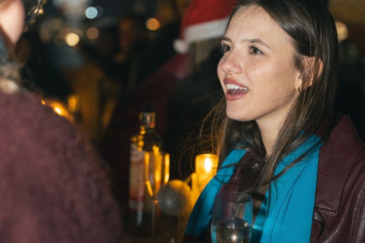Woman in blue scarf holding wine glass at nighttime gathering.