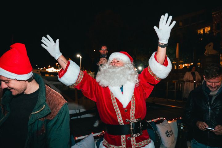 Person in Santa suit with arms raised at night, surrounded by people.