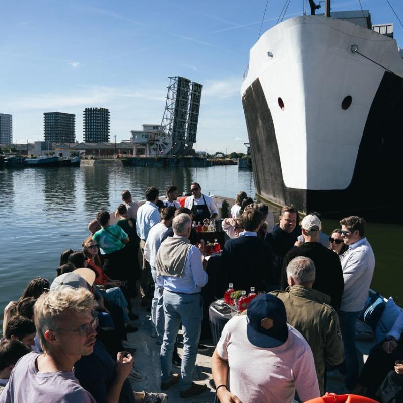 People socializing on a boat next to a large docked ship on a sunny day.