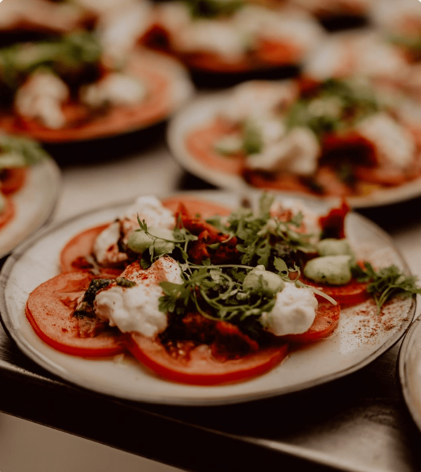 Plates of sliced tomatoes topped with herbs, cream, and greens.