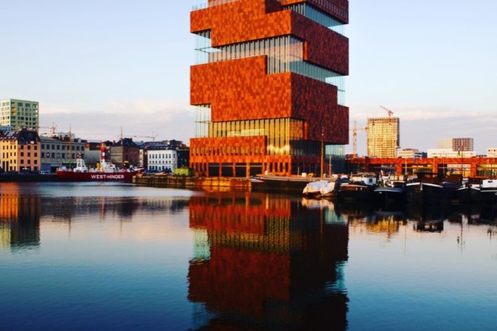 Modern stacked brick building reflecting on calm waterfront at sunset.