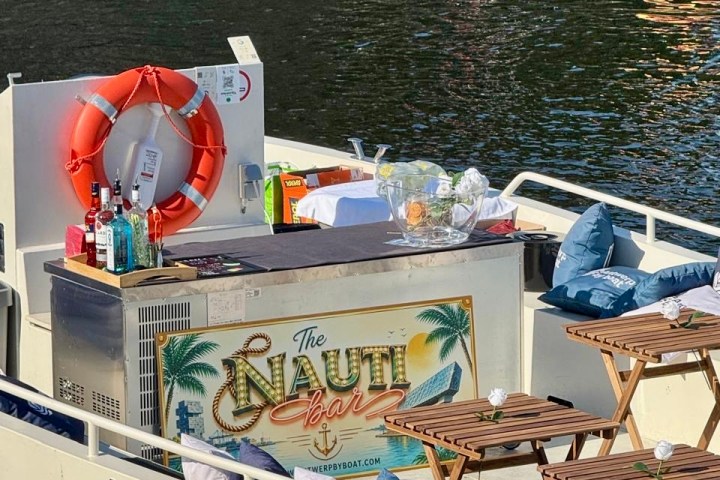 Floating bar with drinks setup and nautical decor on a boat next to a river.