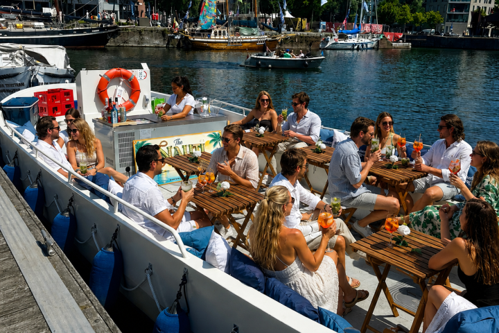 Group of people dining on a boat docked by waterfront buildings.