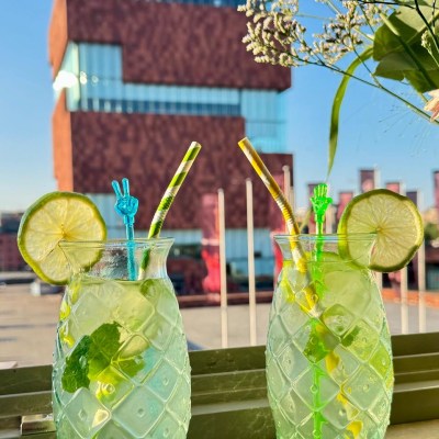 Two lime-mint drinks with straws, city building background.