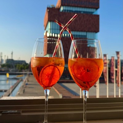 Two Aperol Spritz glasses on a ledge with a building in the background.