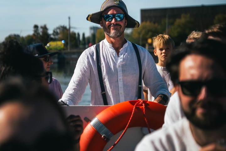 Person in sunglasses and hat on boat, holding life preserver; others around.