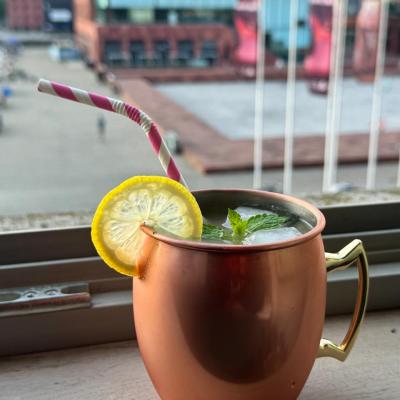 Copper mug with lemon slice and straw, cityscape background.
